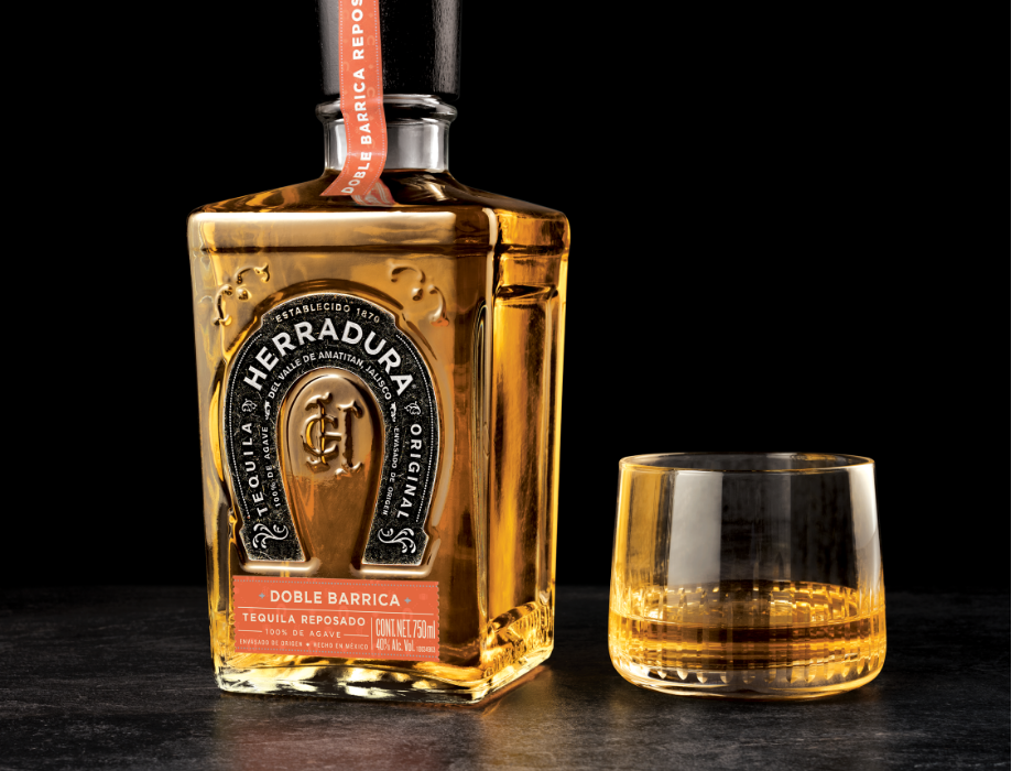 A bottle of Herradura Double Barrica beside a partially filled glass.